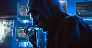 A hacker wearing a mask to cover his face is using computer to hack data to get ransom from victims.